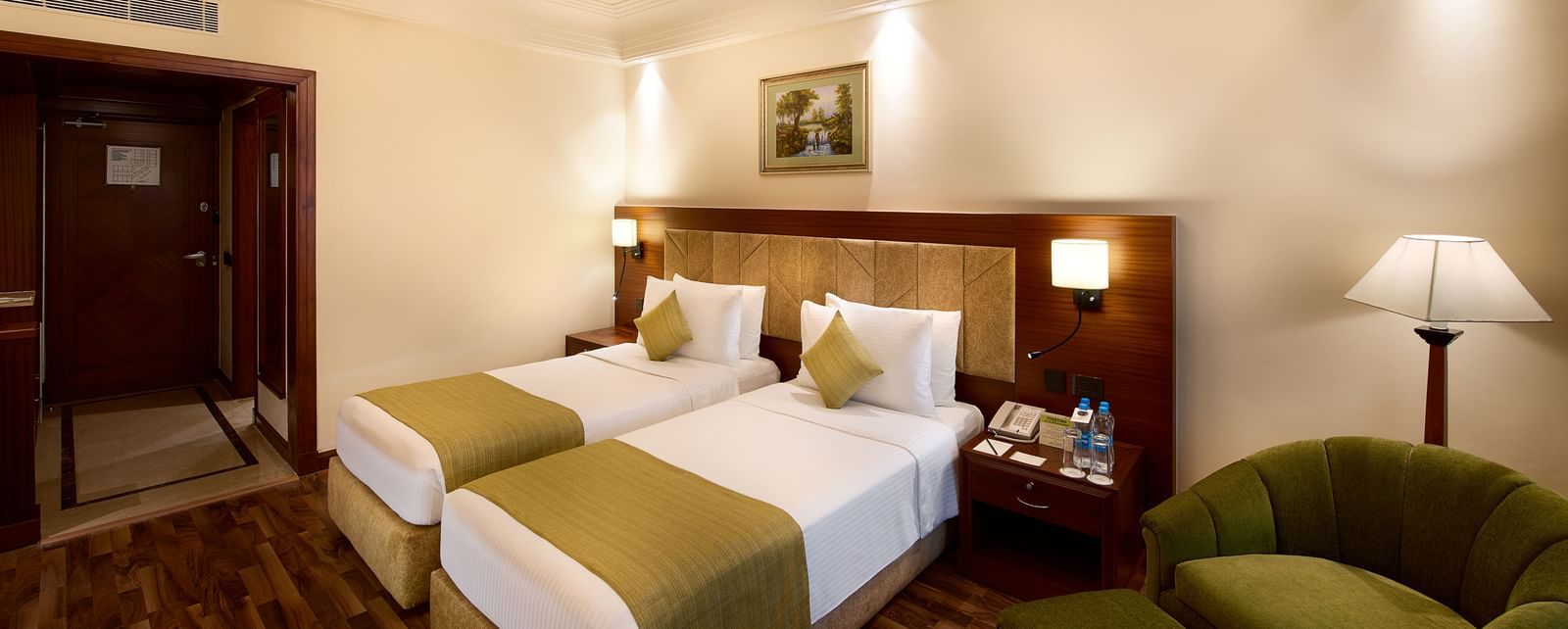 An image of a bedroom featuring twin bed, a sofa chairs, and a bedside table with lamp - Accord Hotels and Resorts